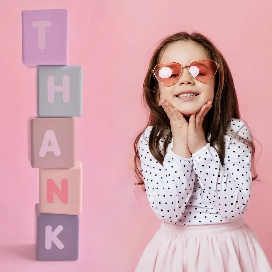 Danke Frau Doz. Lechner ! Ein Mädchen mit Sonnenbrille lächelt, umgeben von bunten Bauklötzen mit dem Wort „THANK“.